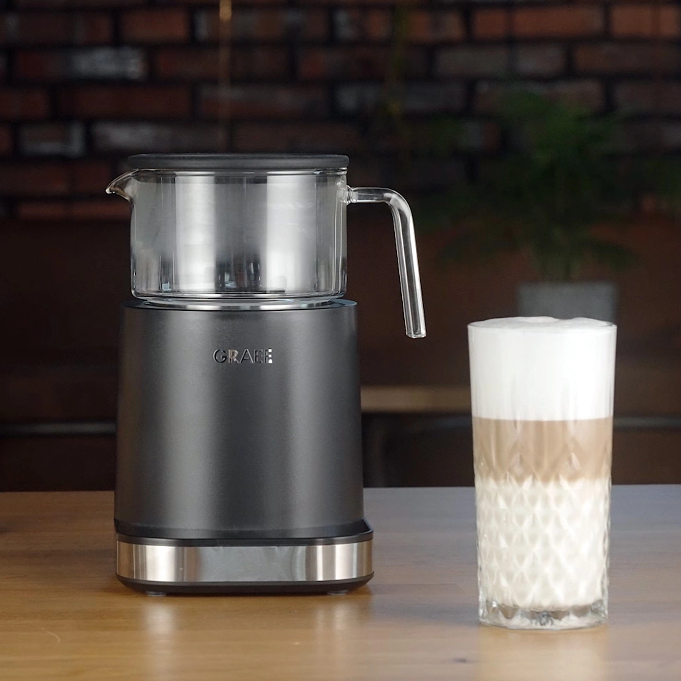 Milchaufschäumer mit Glasbehälter und Latte Macchiato daneben.