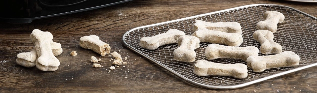 Hunde-Kekse in Knochenform auf einem Holzbrett und Gitter