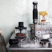 Küchenutensilien auf einem Tisch: Mixer, Behälter, Milch, Nüsse, Schneebesen.