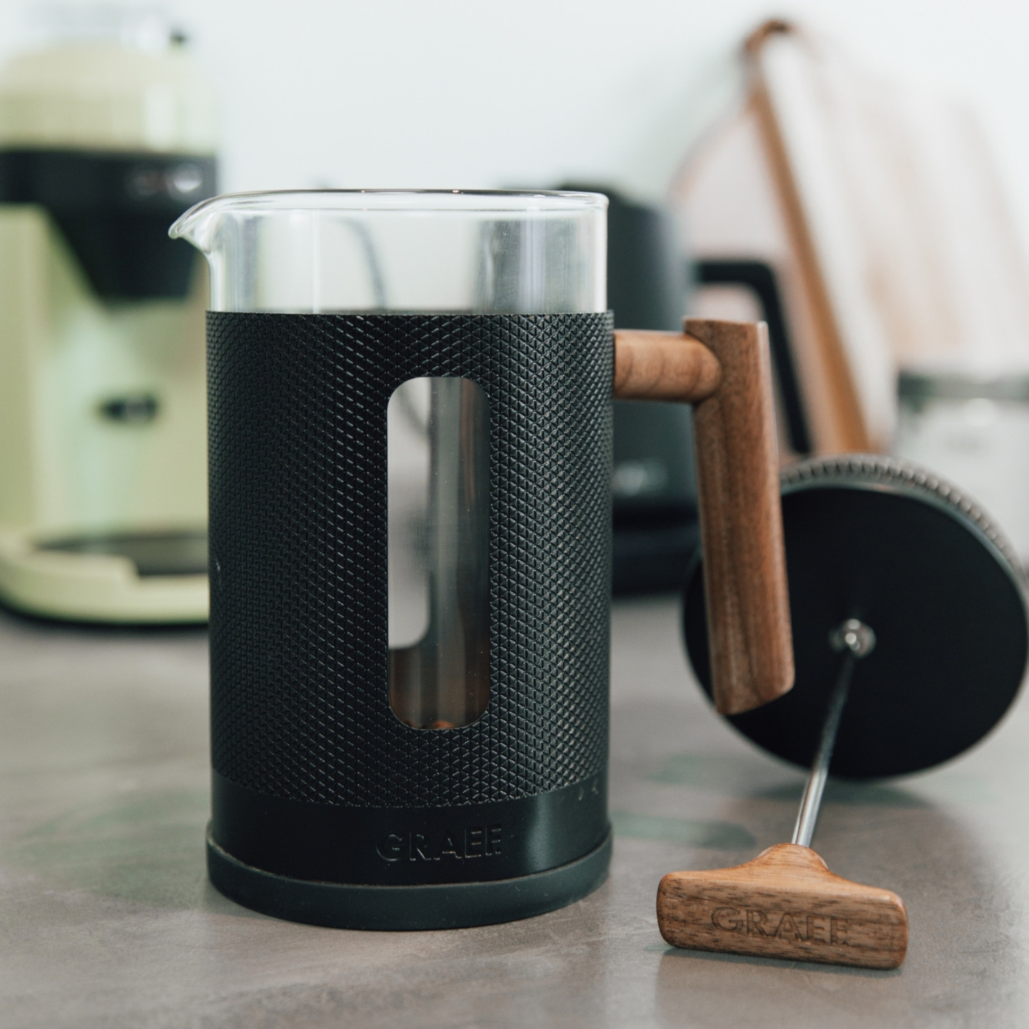 Coffee press with wooden handle and black casing on a gray surface, close-up shot.