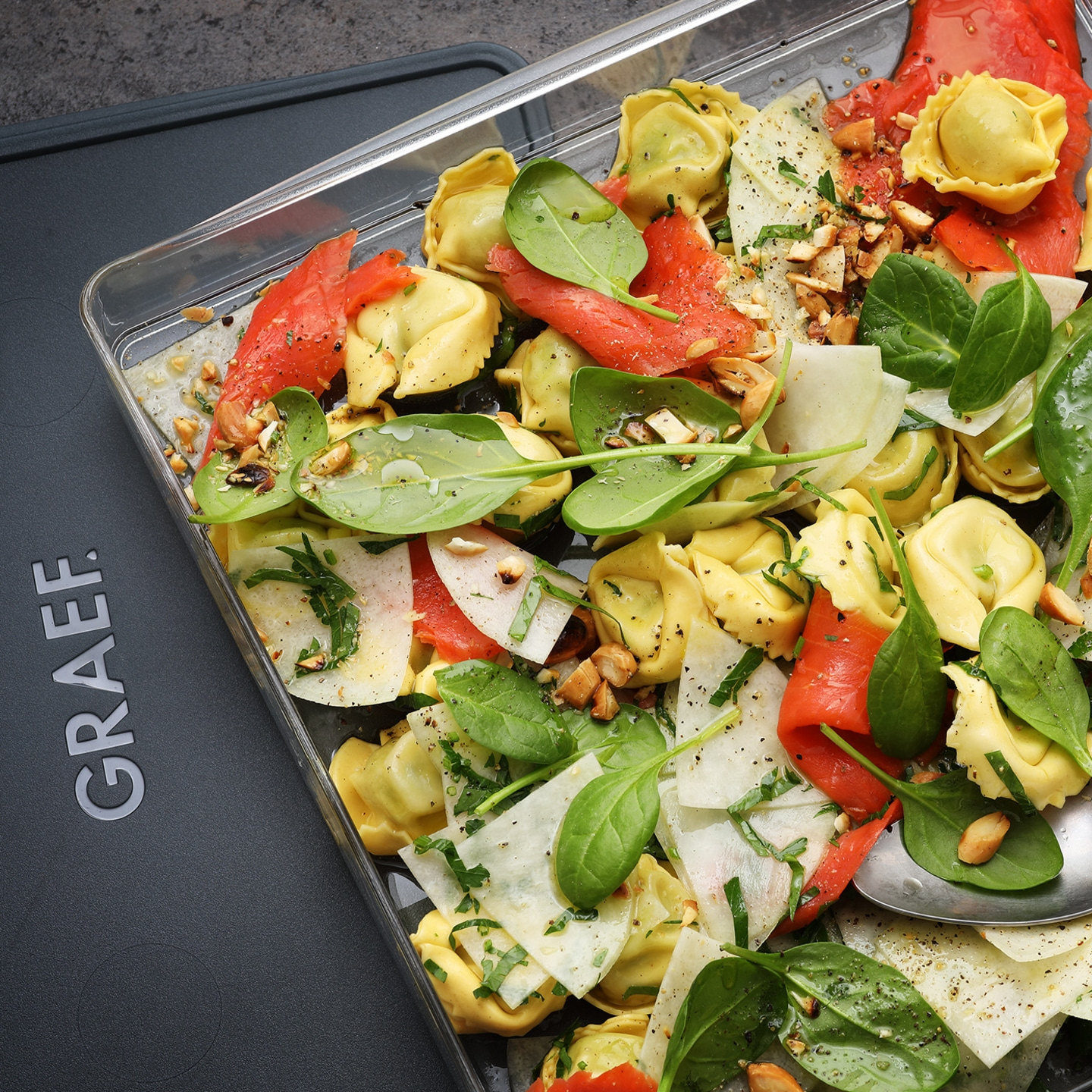 Tortellini-Salat mit Lachs, Spinat, Nüssen und Käse in einer Schale