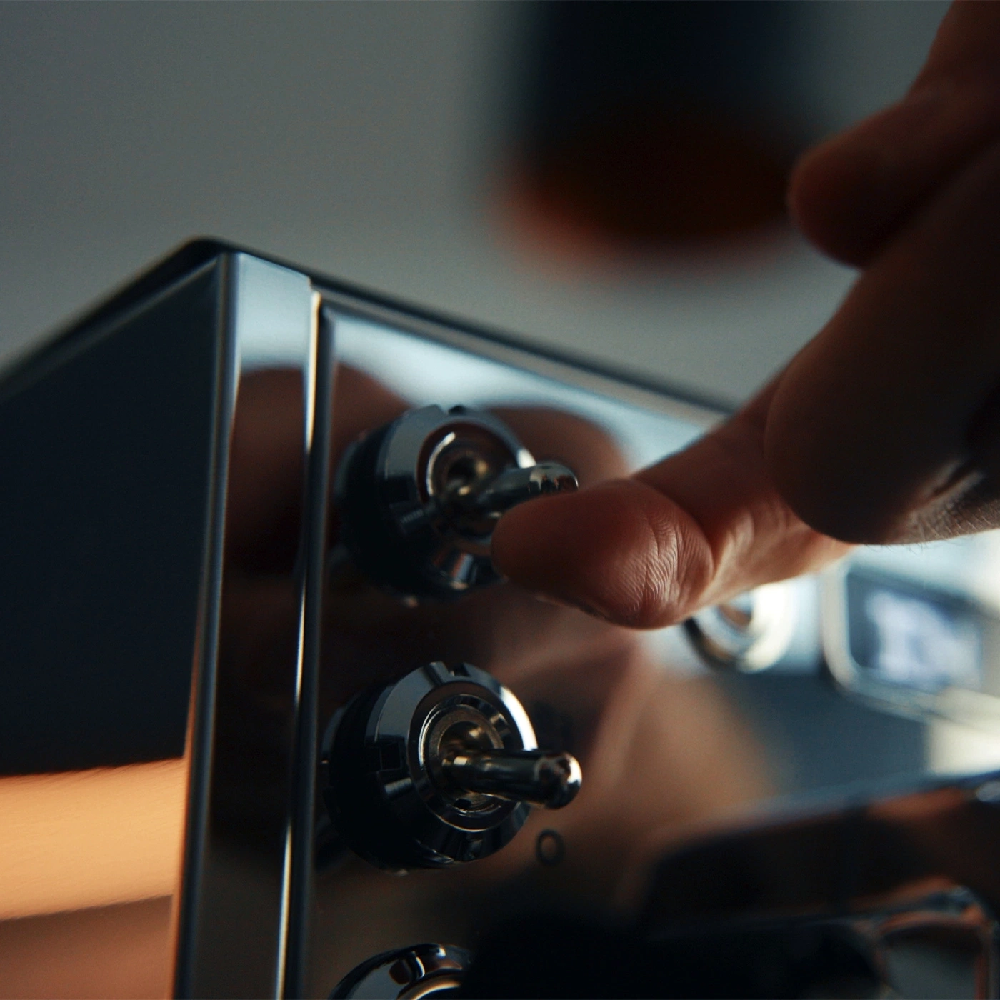 A hand operates a toggle switch on a shiny appliance.