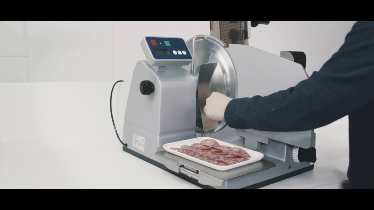 Fleischschneidemaschine schneidet Salami. Person bedient die Maschine. Auf Tablett liegen Scheiben.