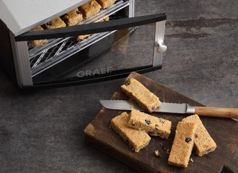 Getrocknete Lebensmittel und Messer auf einem Holzbrett neben einem Trockner.