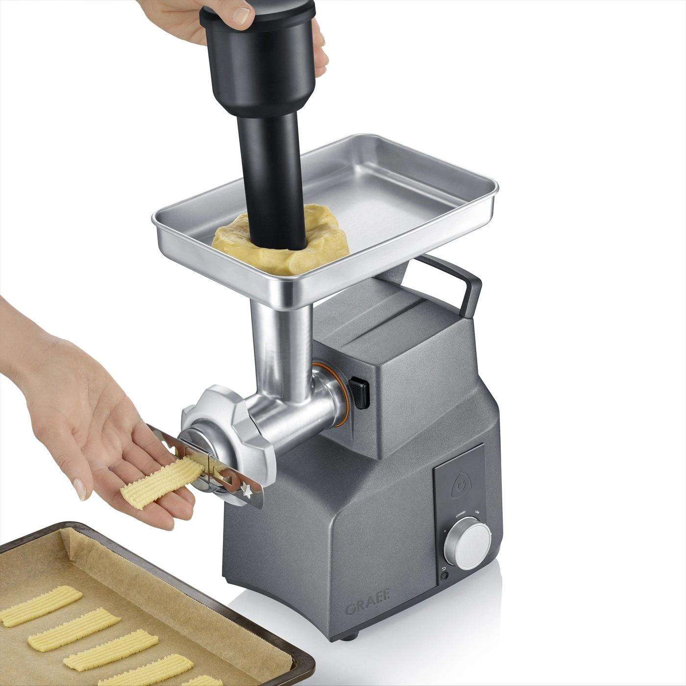 A hand pushes dough into a cookie press, forming cookies onto a baking sheet.