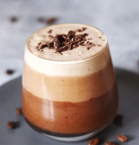 Dreifarbiger Kaffee mit Schokoladenstückchen auf einem grauen Teller