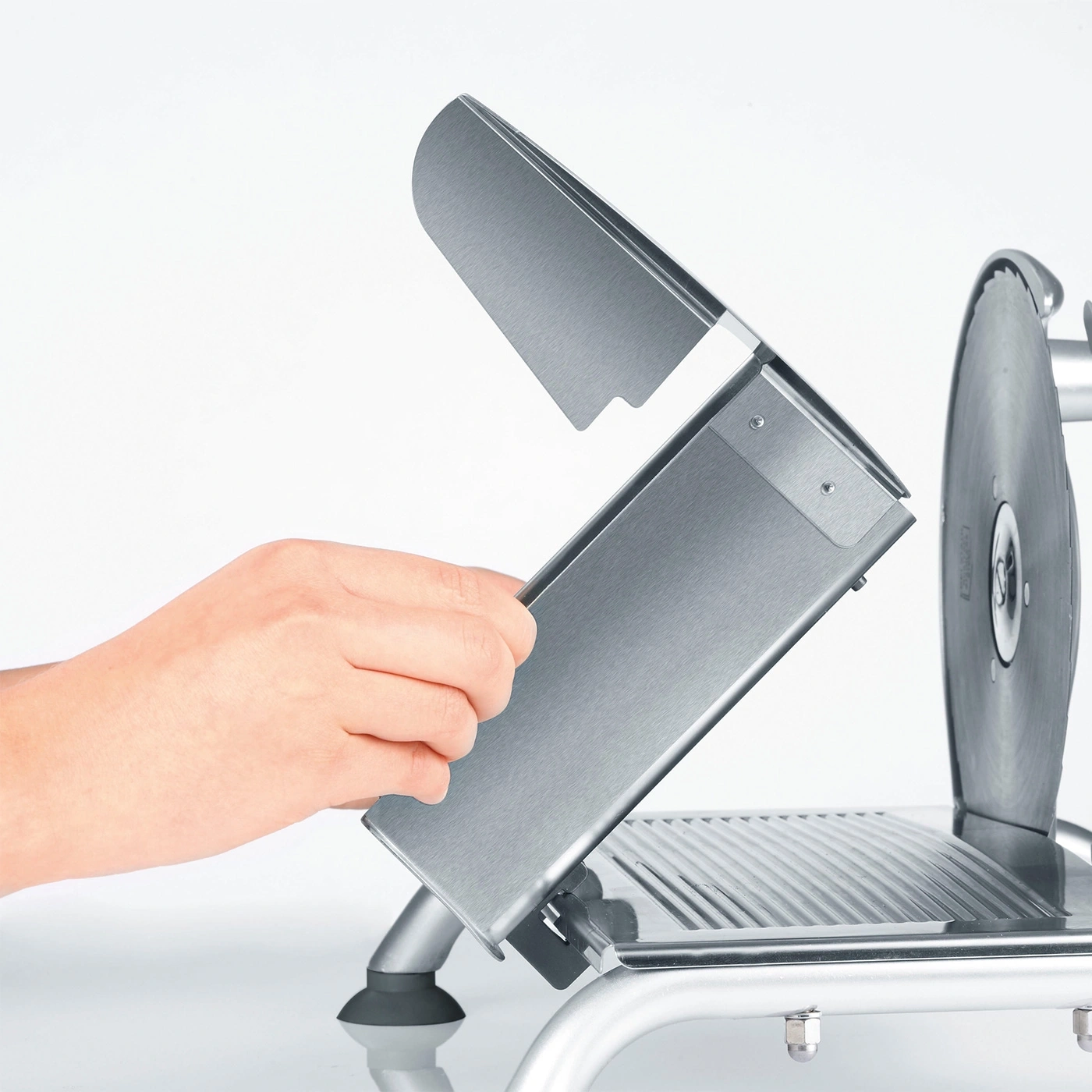 Close-up of a meat slicer with open guard and a hand holding it