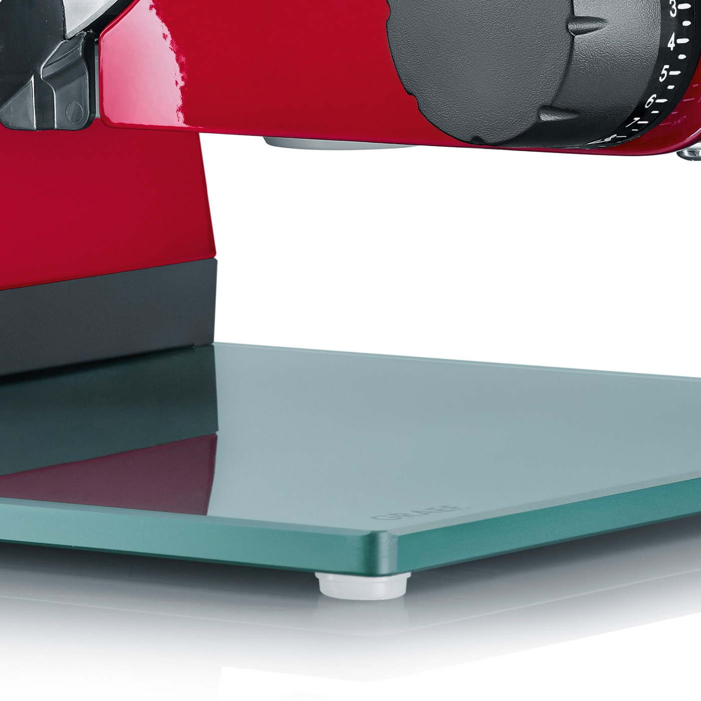 Close-up of a red meat slicer with a glass plate and adjustment dial.