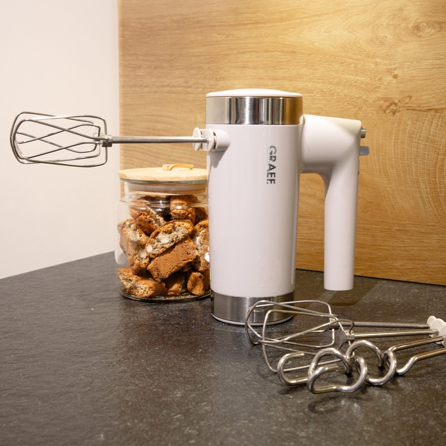 Handrührgerät mit Zubehör und Keksen in einem Glas auf einer Arbeitsplatte