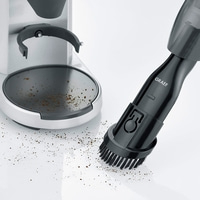 Kaffeemühle und Staubsauger mit Bürste reinigen Kaffeepulver auf weißem Untergrund.