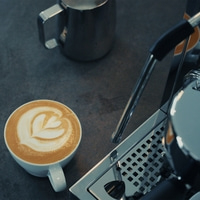 A cup of latte art coffee next to an espresso machine and a milk pitcher.