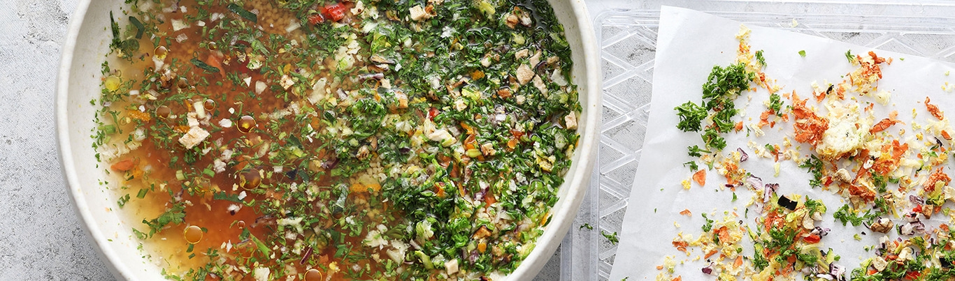 Schüssel mit Suppe und Gemüse, daneben Gemüse auf Papier