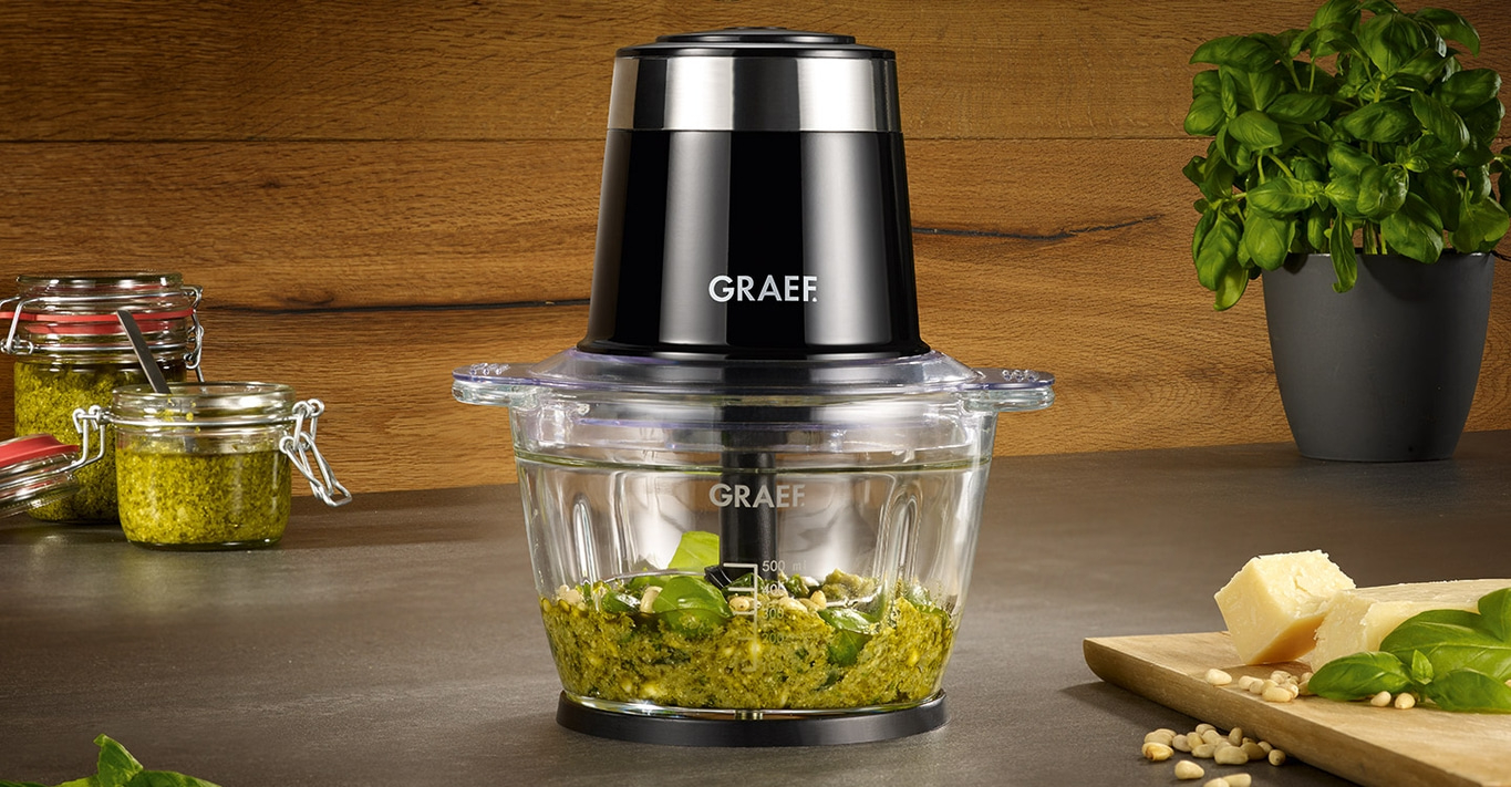 Küchenmaschine mit Pesto, Basilikum, Käse und Pinienkernen auf Holzbrett