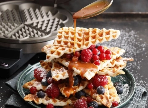 Waffeln mit Beeren und Karamellsauce, die auf einem Teller serviert werden.