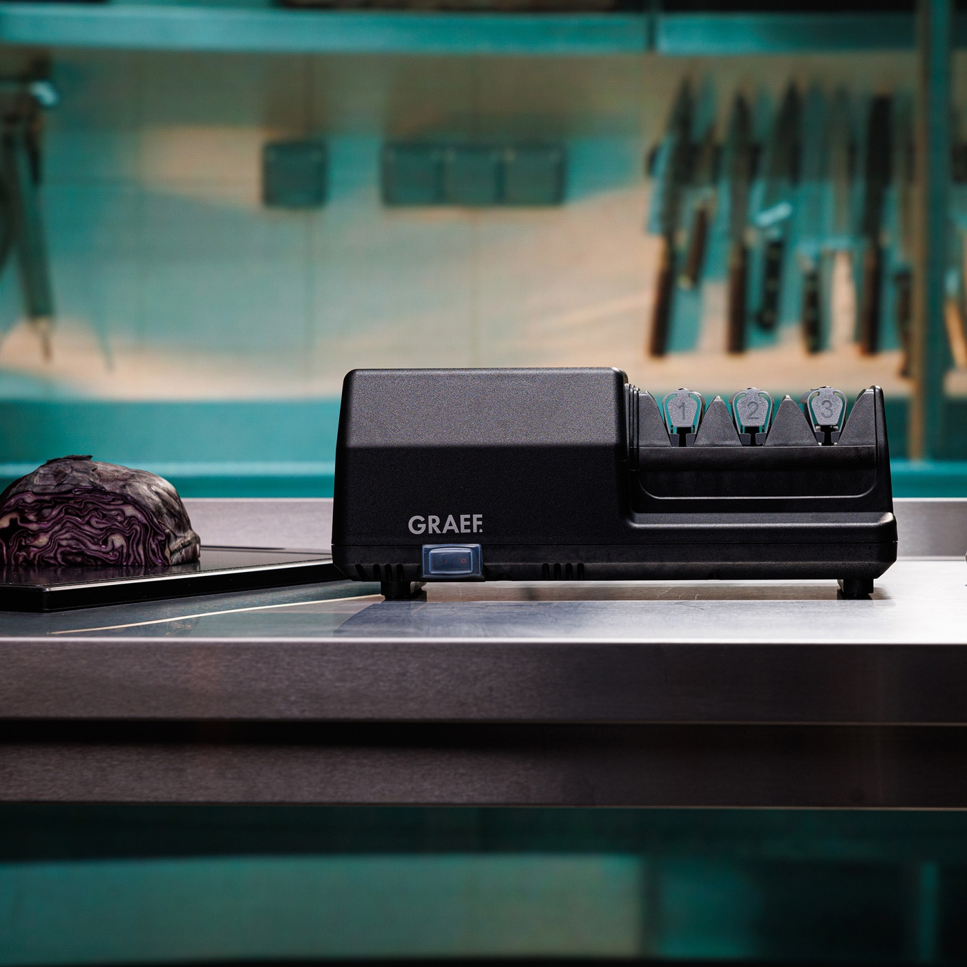 Black knife sharpener with vegetables on a metal surface in the kitchen.