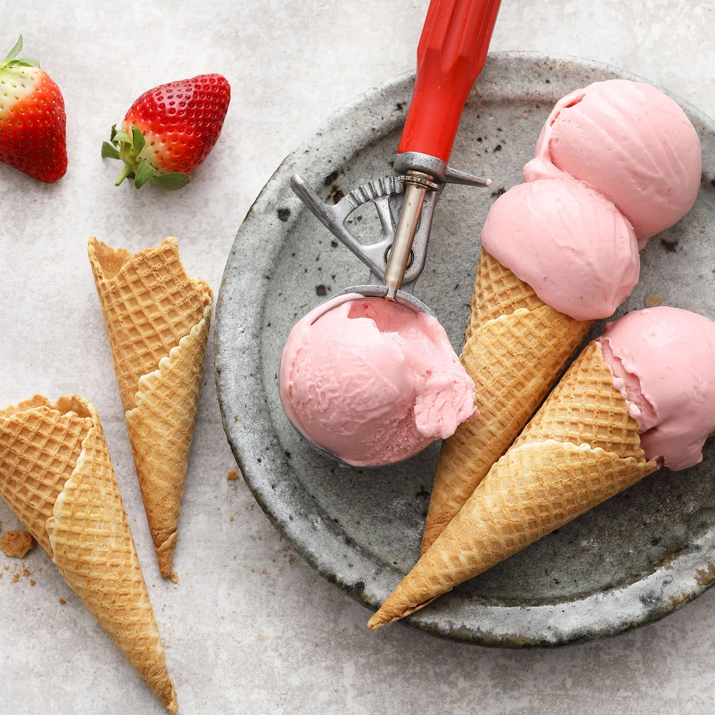 Erdbeer-Eiscreme in Waffelkegeln auf einem Teller mit Löffel und Erdbeeren.