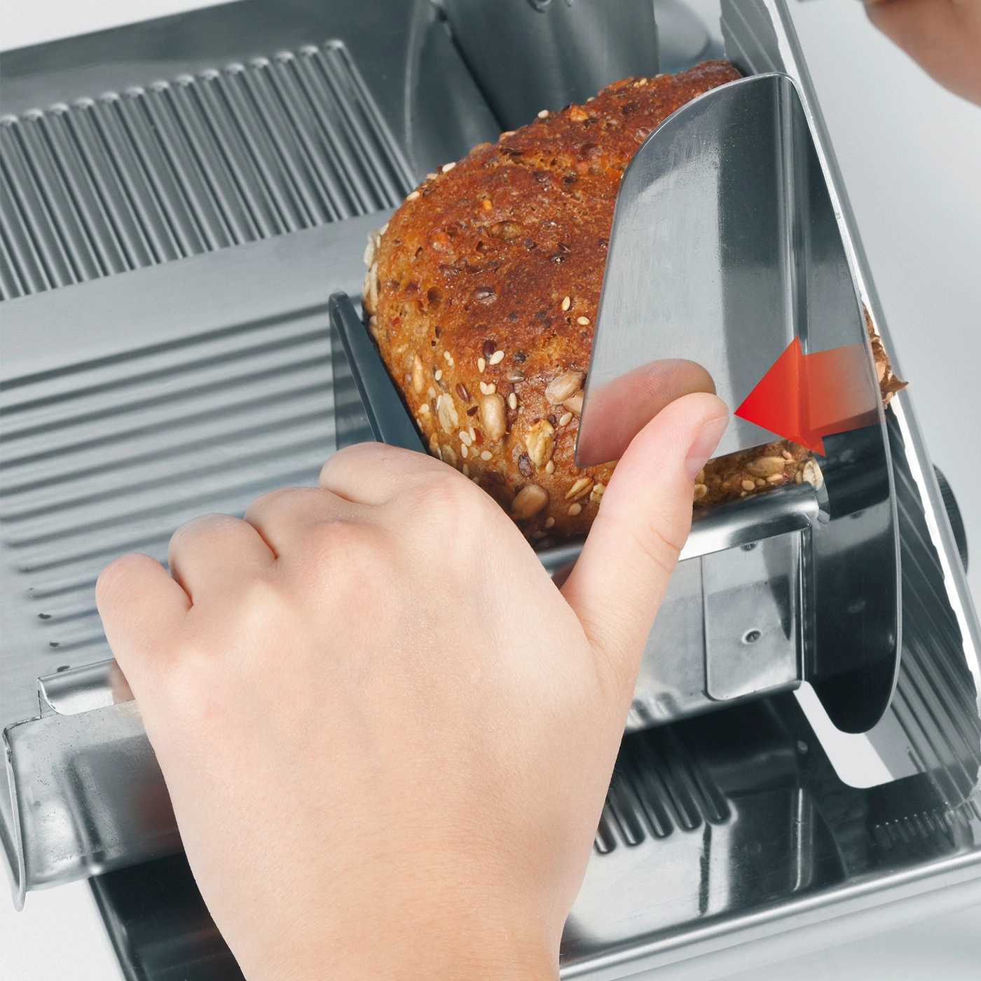 Close-up of hand slicing bread with a bread slicer, red arrow indicates direction.