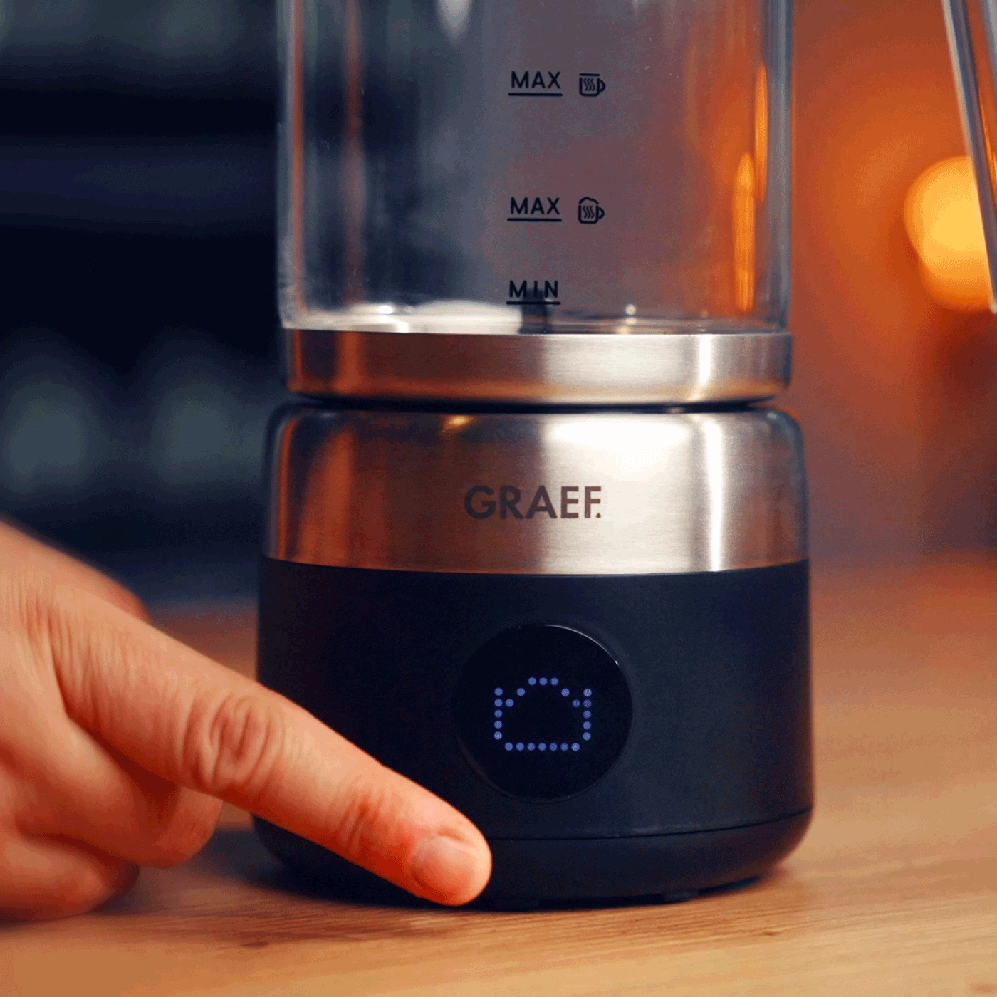 Ein Finger drückt auf die Anzeigeeinheit eines Wasserkochers von Graef.