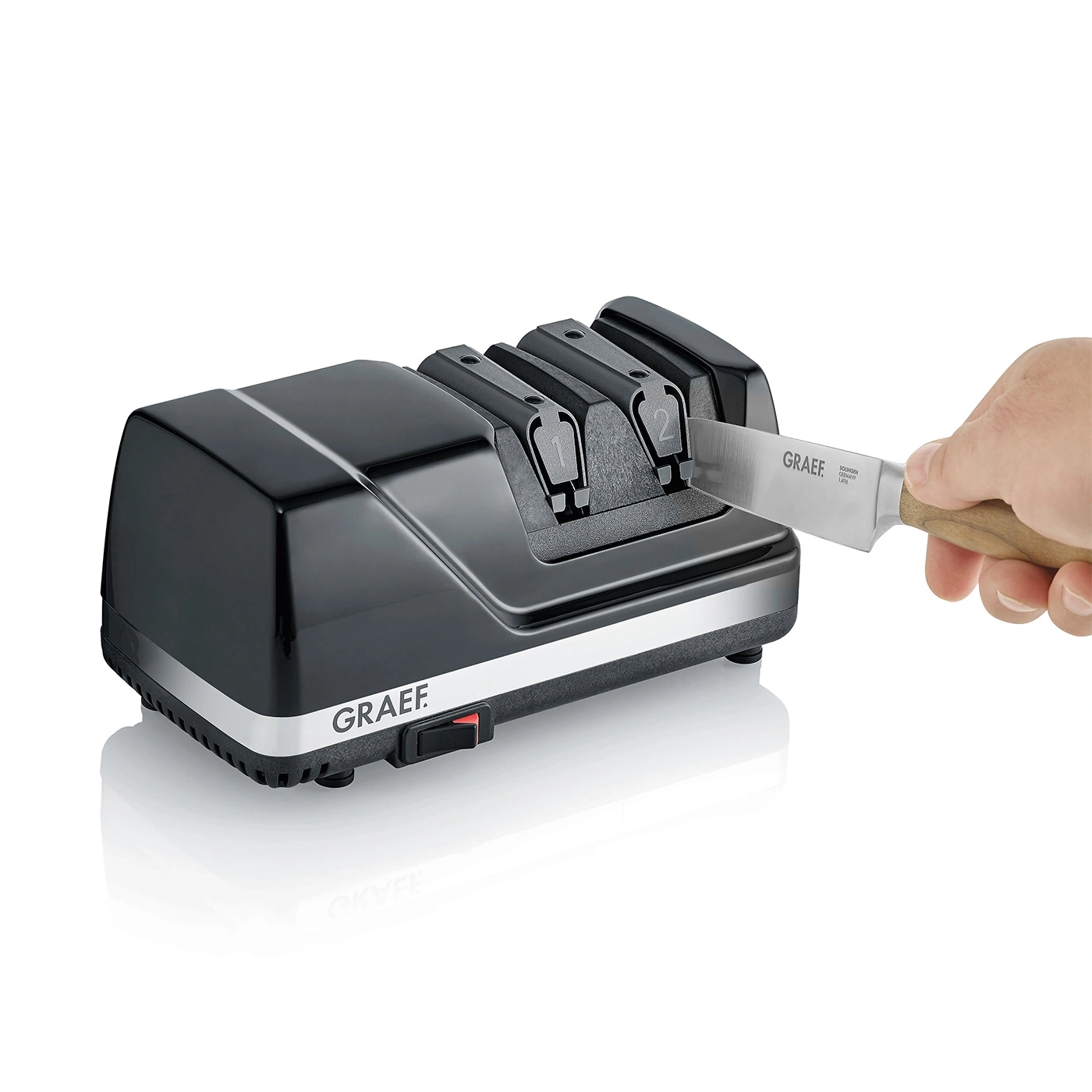Black electric knife sharpener with knife and hand, GRAEF brand, product shot.