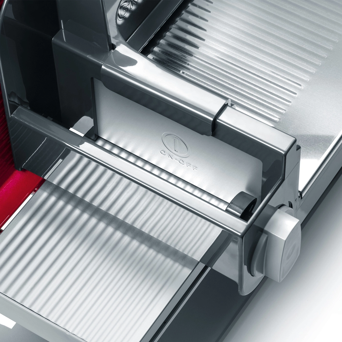 Close-up of a silver meat slicer with an on-off switch and a red part.