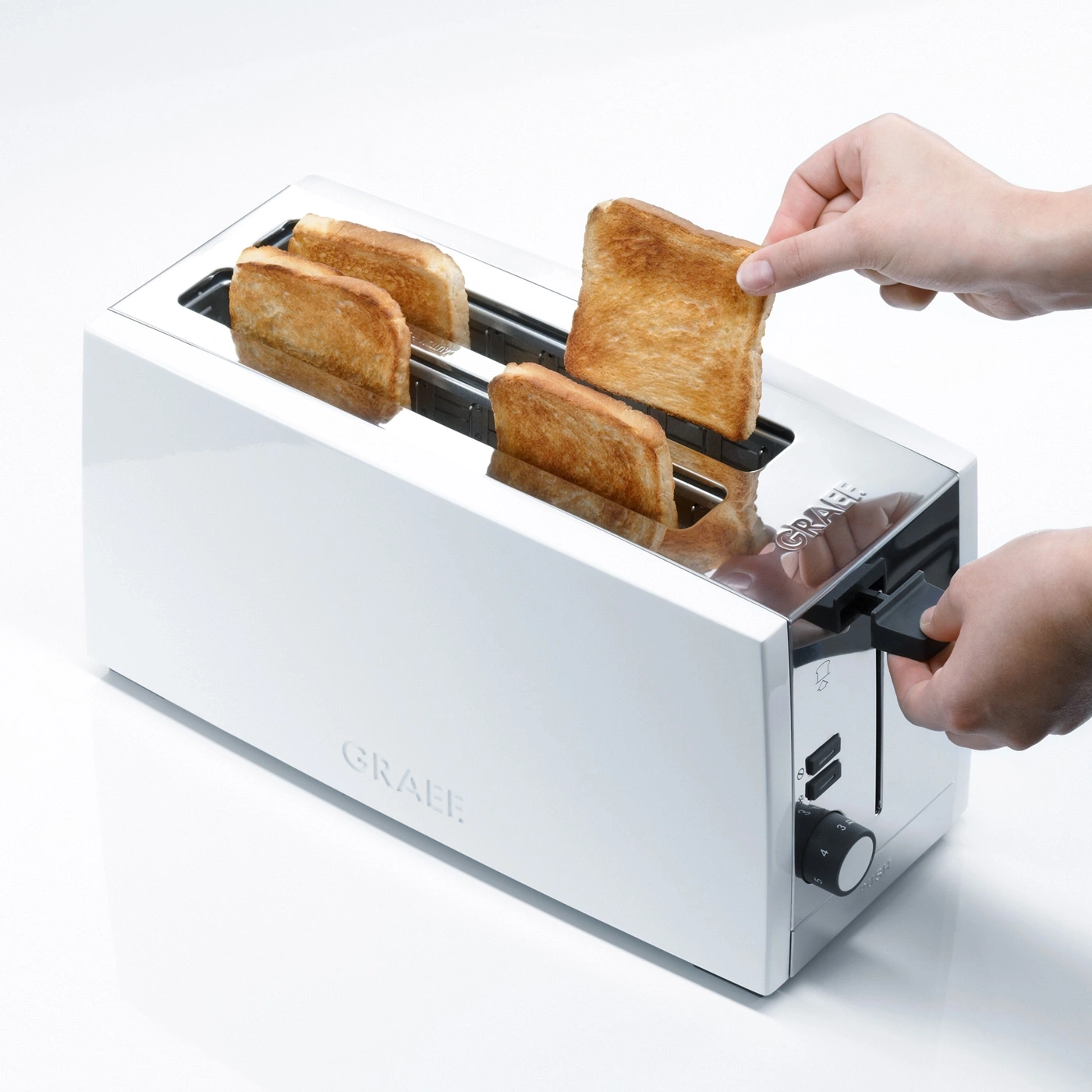Eine Hand nimmt Toast aus einem weißen Toaster mit vier Scheiben Toast.