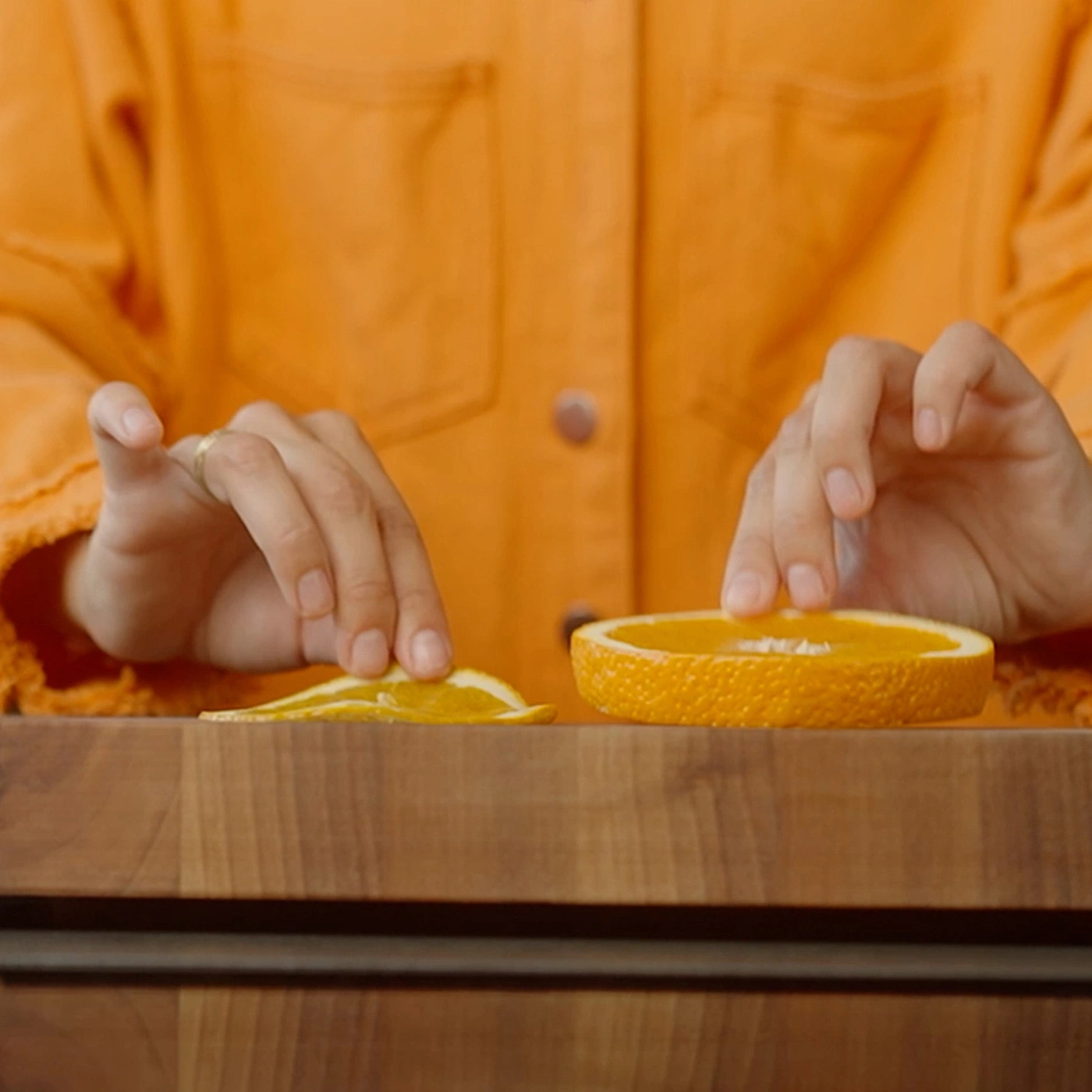 Person arranging orange slices on a wooden table, one thin and one thick slice.