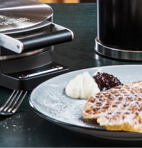 Waffeleisen mit Waffel, Sahne und Marmelade auf einem Teller