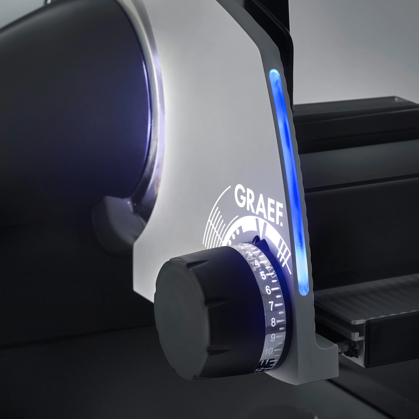 Close-up of a black and gray meat slicer with blue lighting and GRAEF logo
