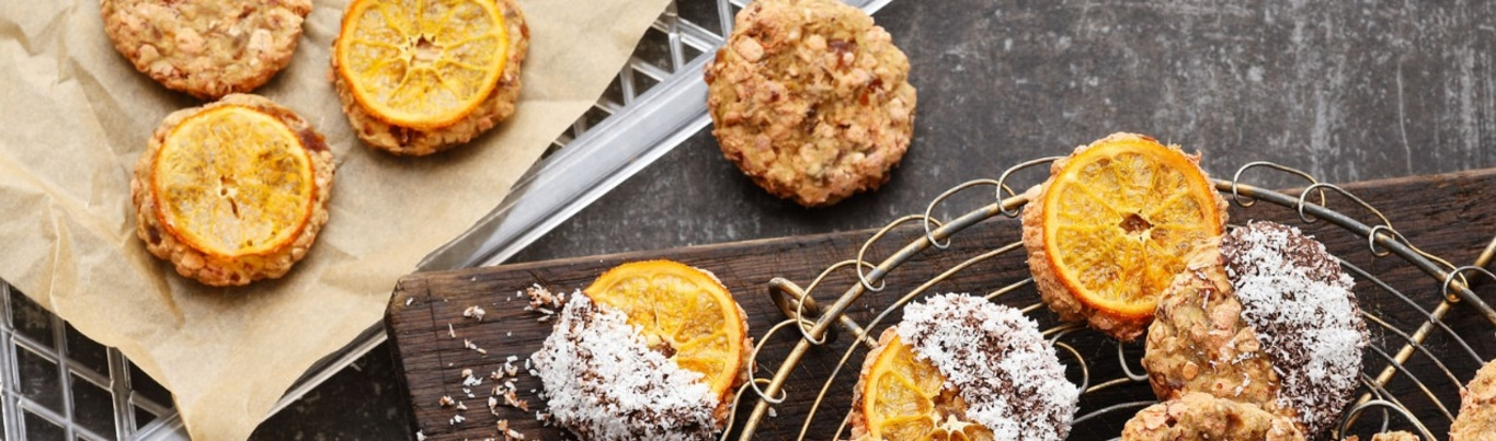 Kekse mit Orangenscheiben und Kokosraspeln auf Holzbrett und Gitter