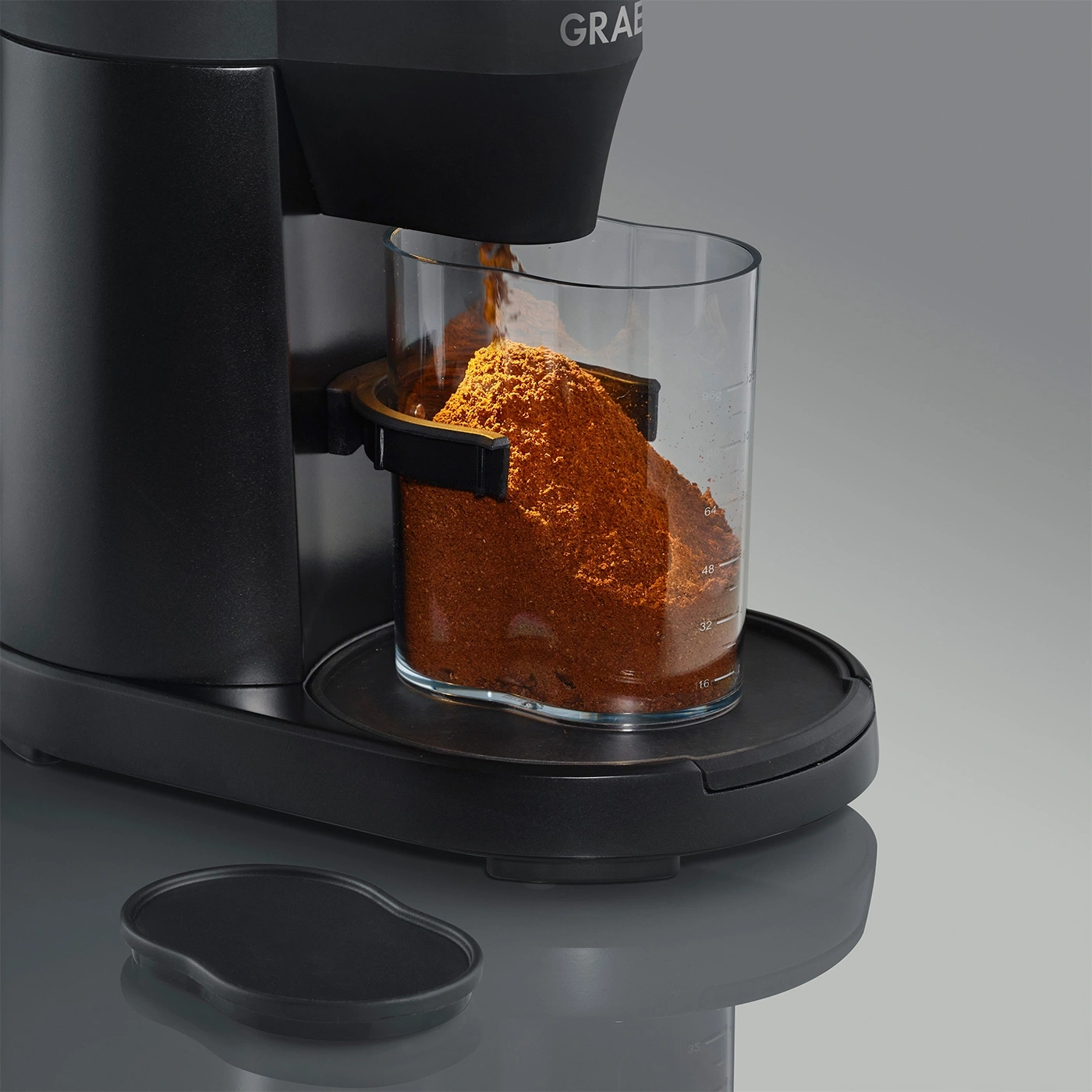Coffee grinder with glass container filled with coffee powder, black design, close-up shot