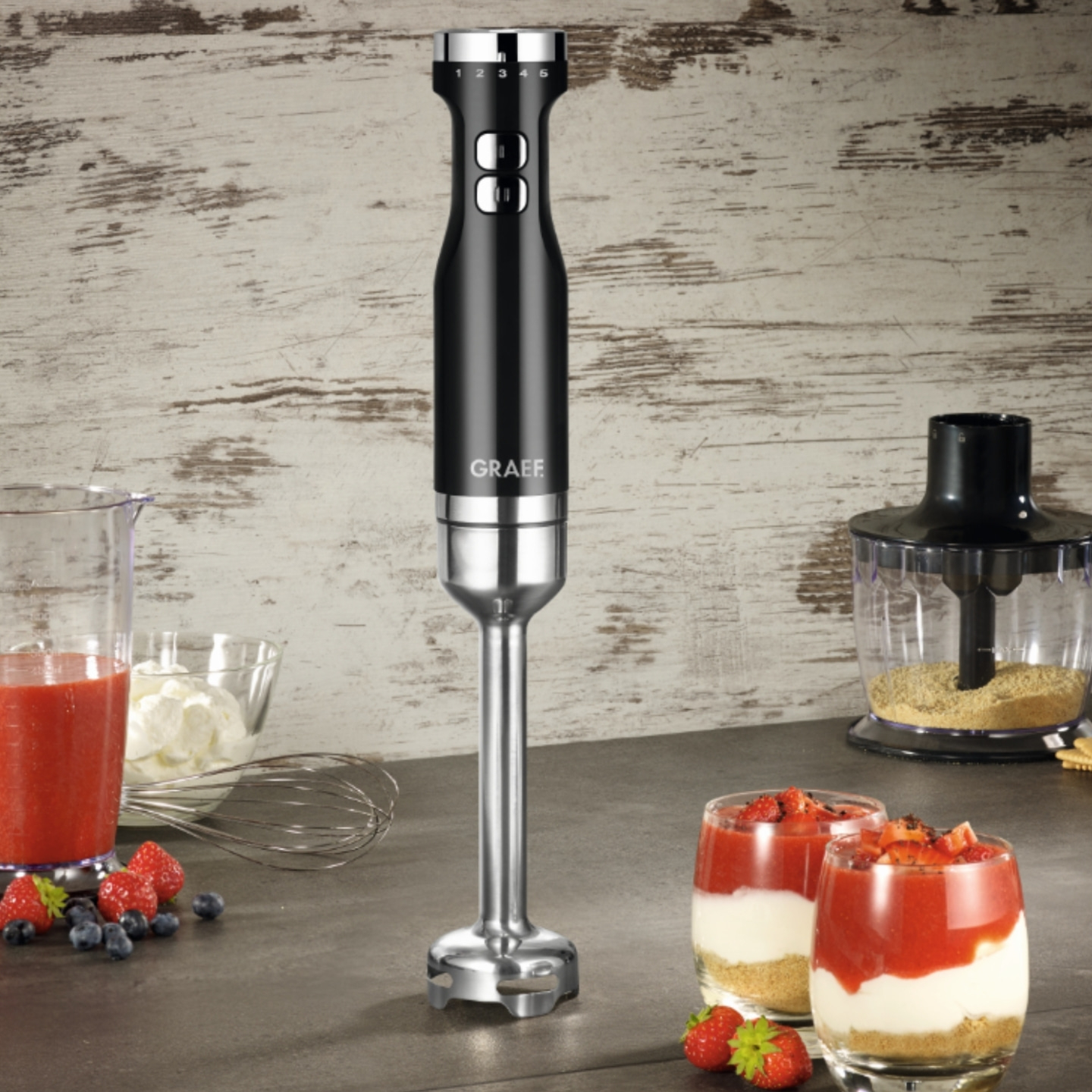 Schwarzer Stabmixer mit Essen und Früchten auf dem Tisch.