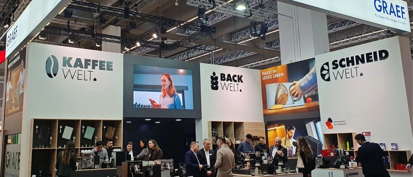Coffee and baking world booth with people and logos.