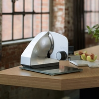 A silver Graef slicer on a wooden table with melon slices.