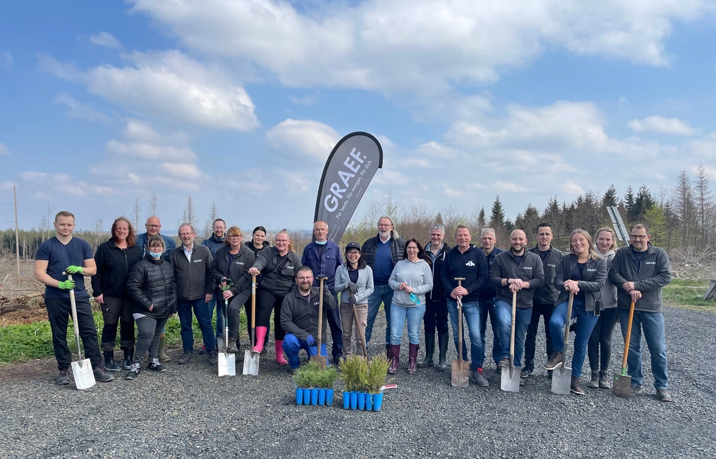 Group of people with shovels in front of trees and blue sky