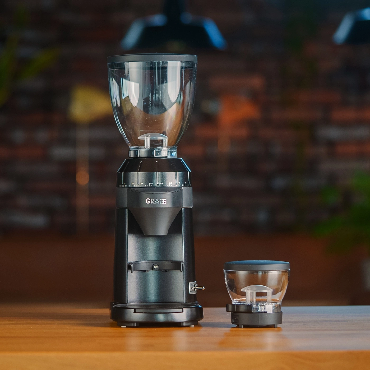Two black coffee grinders, one large and one small, on a wooden table.