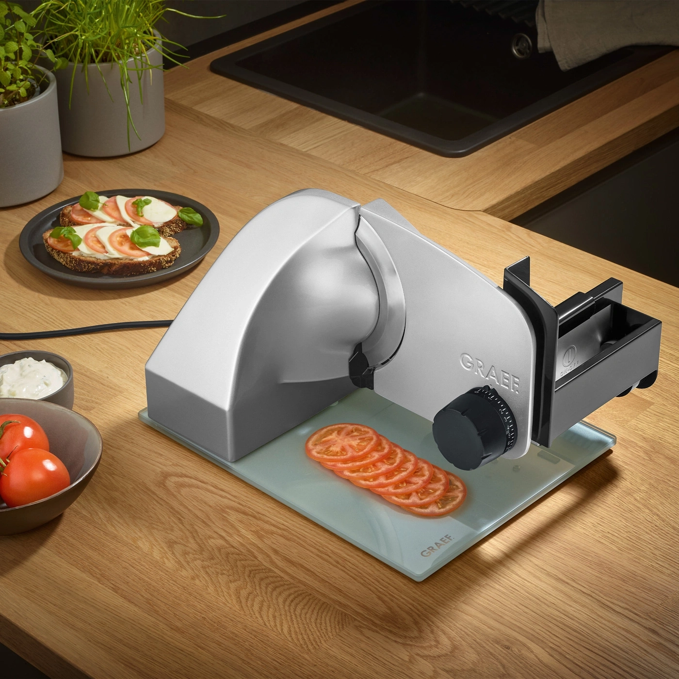 Tomato slices on cutting board next to slicer and food on a plate
