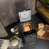 Bread maker with bread, ingredients, and loaves on a black table