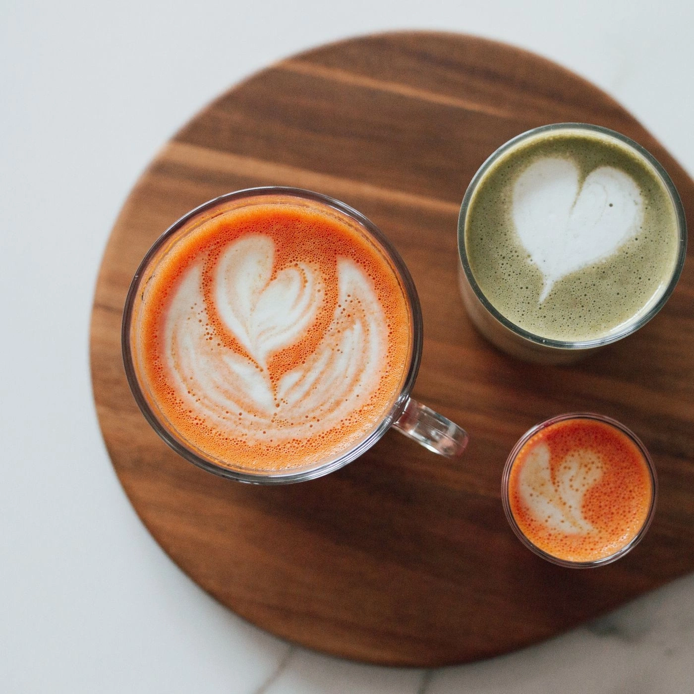 Drei Getränke mit Latte Art auf einem Holzbrett, Draufsicht.