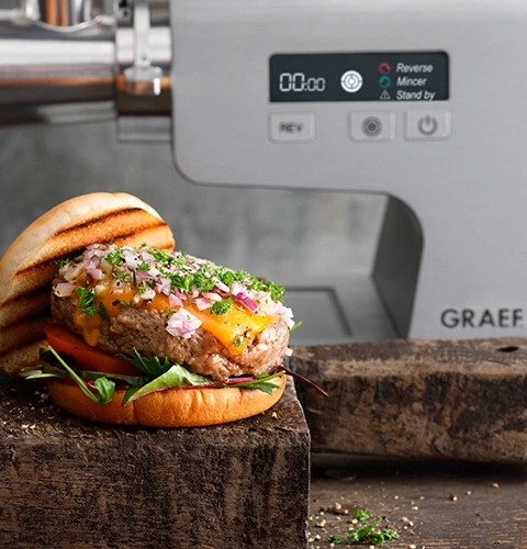 Burger mit Käse und Zwiebeln vor Fleischwolf-Maschine