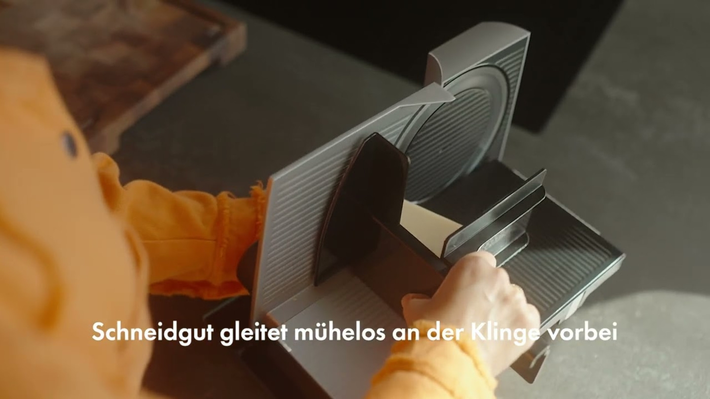 Nahaufnahme einer Person, die eine elektrische Aufschnittmaschine bedient, mit Text.