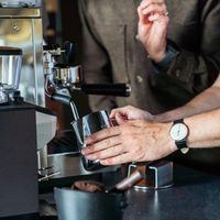 Coffee preparation: Barista pouring milk into a coffee cup with an espresso machine.