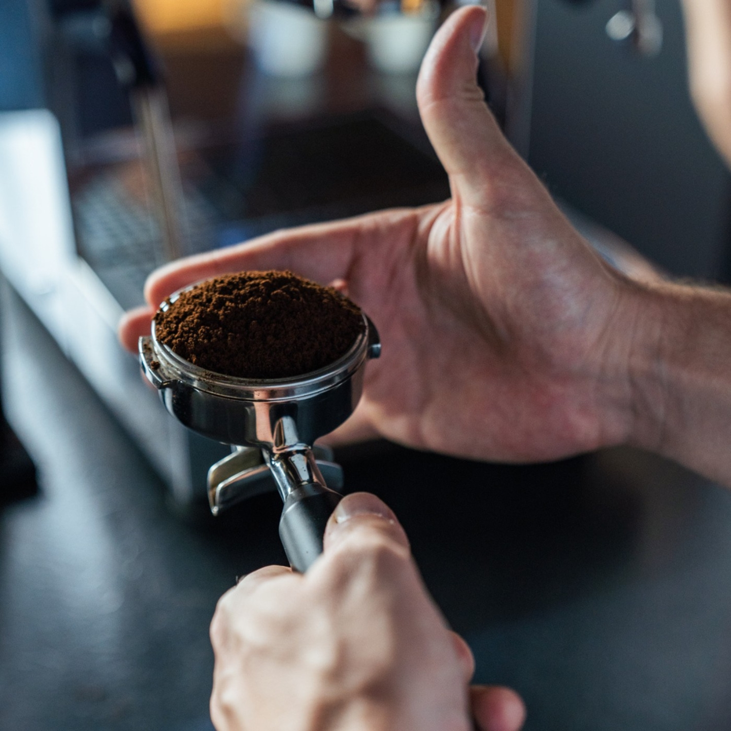 Nahaufnahme von Händen, die einen Siebträger mit Kaffeepulver halten, Kaffeezubereitung
