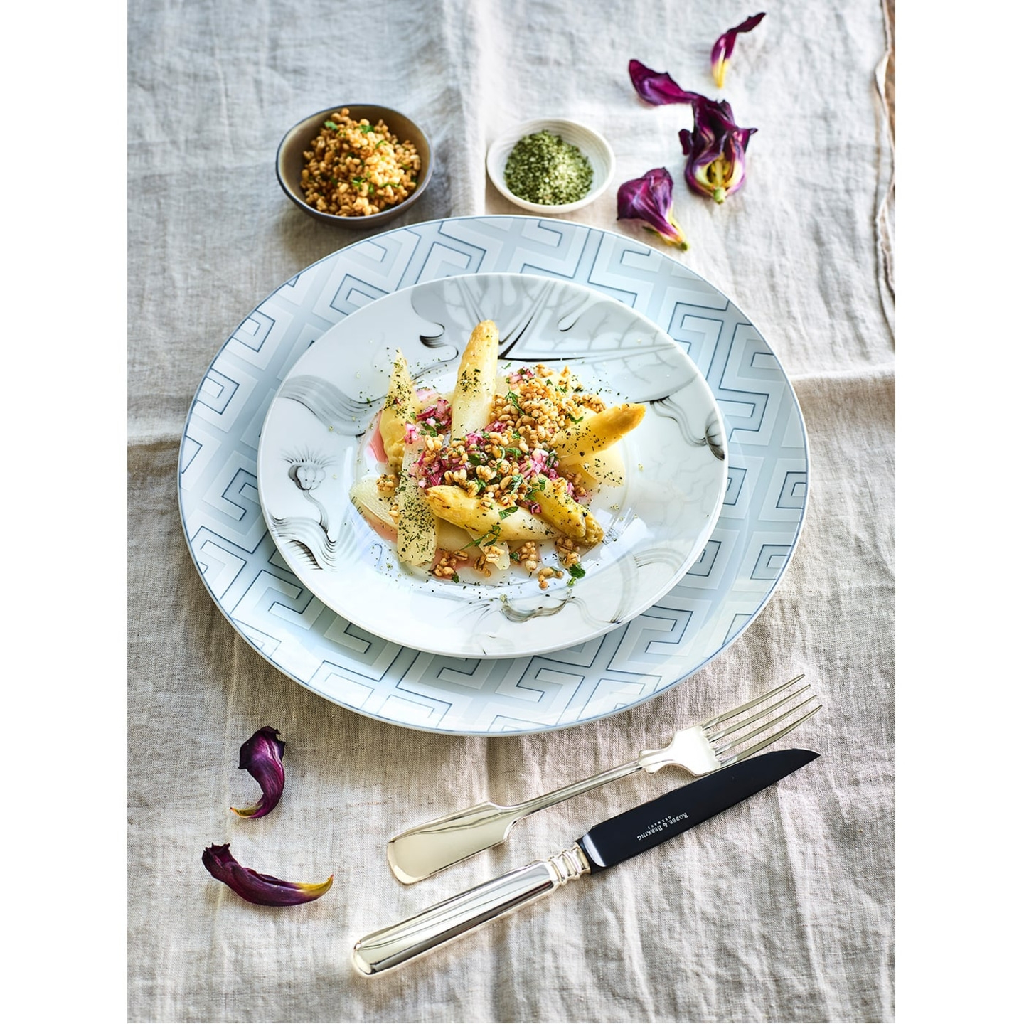 Plate of asparagus dish with cutlery and flowers on linen tablecloth