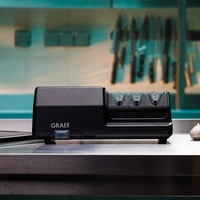 Black knife sharpener with GRAEF logo and numbers 1, 2, 3 on top, on a metal surface.