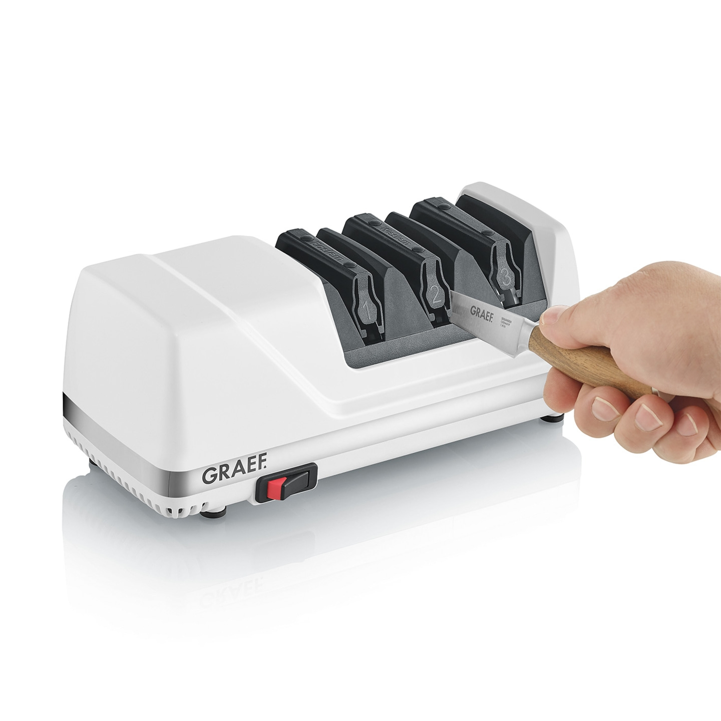 A white electric knife sharpener by Graef with a knife being inserted by a hand.