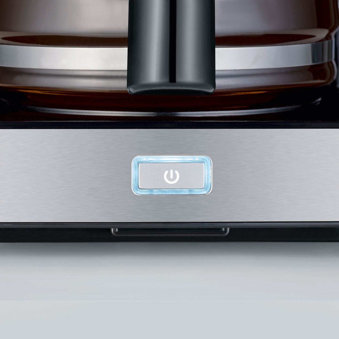 Nahaufnahme eines Kaffeemaschinen-Bedienfelds mit Ein-/Aus-Taste und blauem Licht