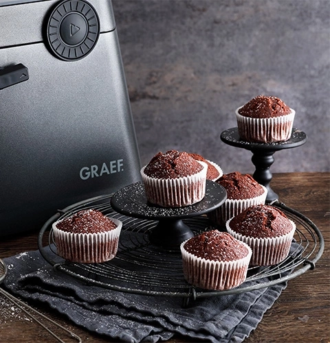 Schokoladenmuffins auf einem Drahtgestell und einem Ständer, neben einem Gerät.