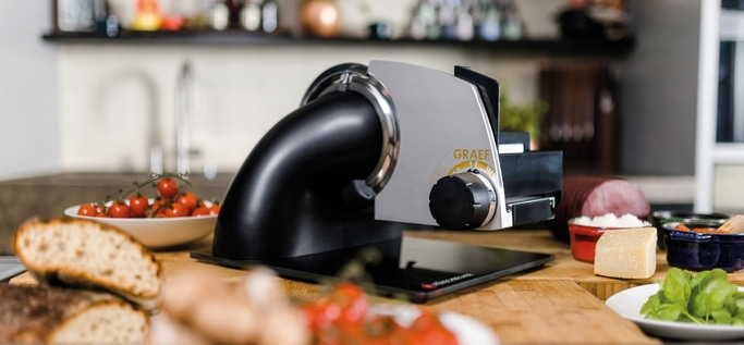 Graef Allesschneider mit Tomaten, Brot, Käse und Wurst auf einem Holztisch