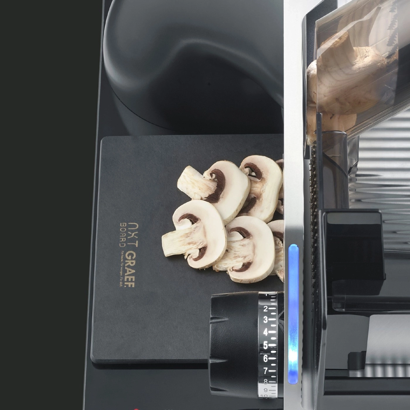 Mushrooms being sliced with a slicer machine on a black cutting board.