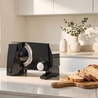 A black bread slicer sits on a countertop next to sliced bread.